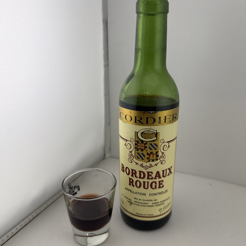 A half bottle of Cordier Bordeaux Rouge wine next to a small glass filled with dark red liquid.