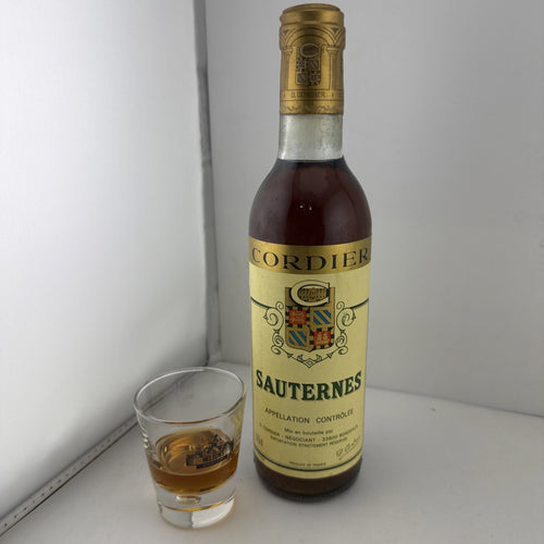A vintage 37.5cl bottle of Cordier Sauternes sweet wine next to a filled shot glass.